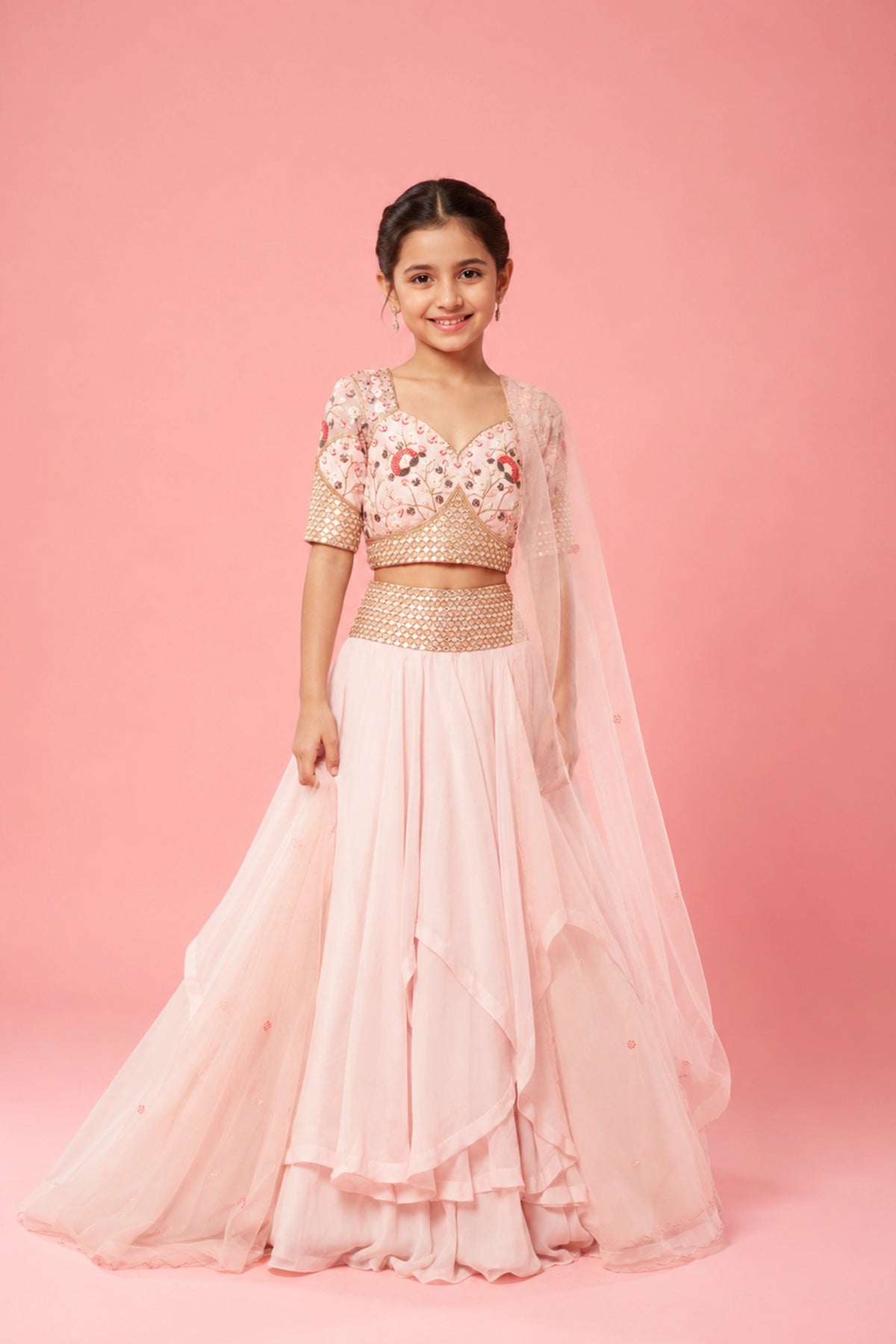 A baby pink layered lehenga crafted in organza, hand embroidery on the blouse, belt, and a soft net dupatta.