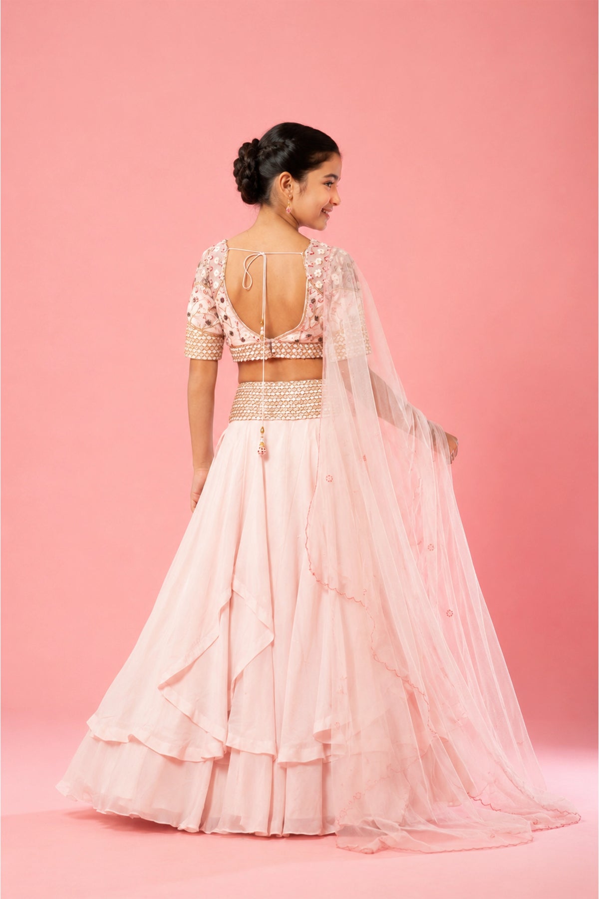 A baby pink layered lehenga crafted in organza, hand embroidery on the blouse, belt, and a soft net dupatta.