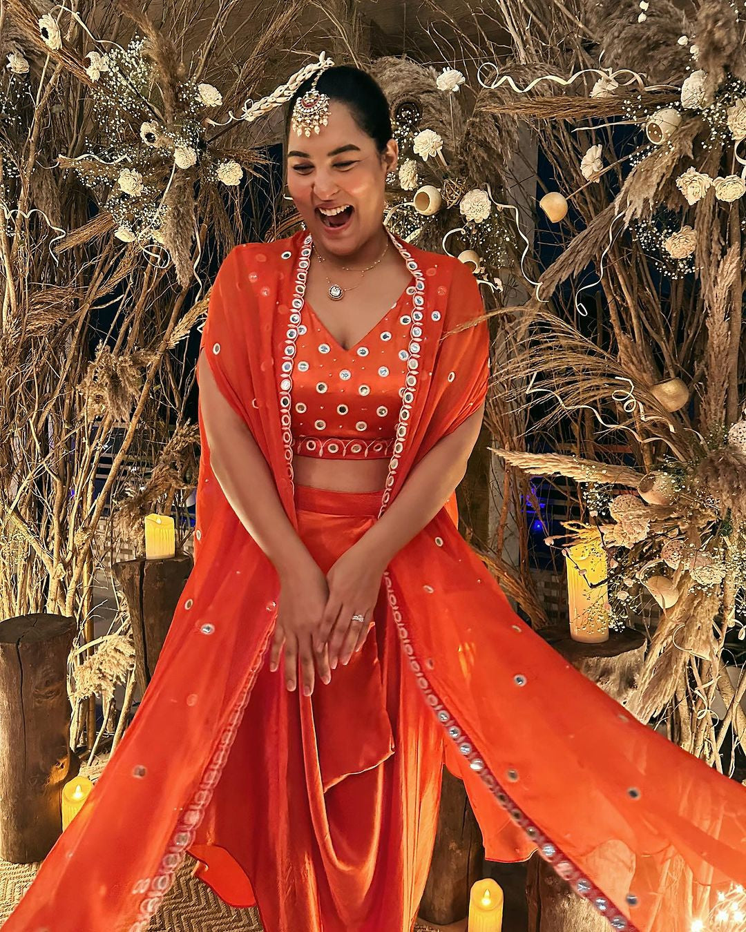 Sakshi Sindhwani wearing a tangerine orange dhoti set with mirror work blouse and cape.