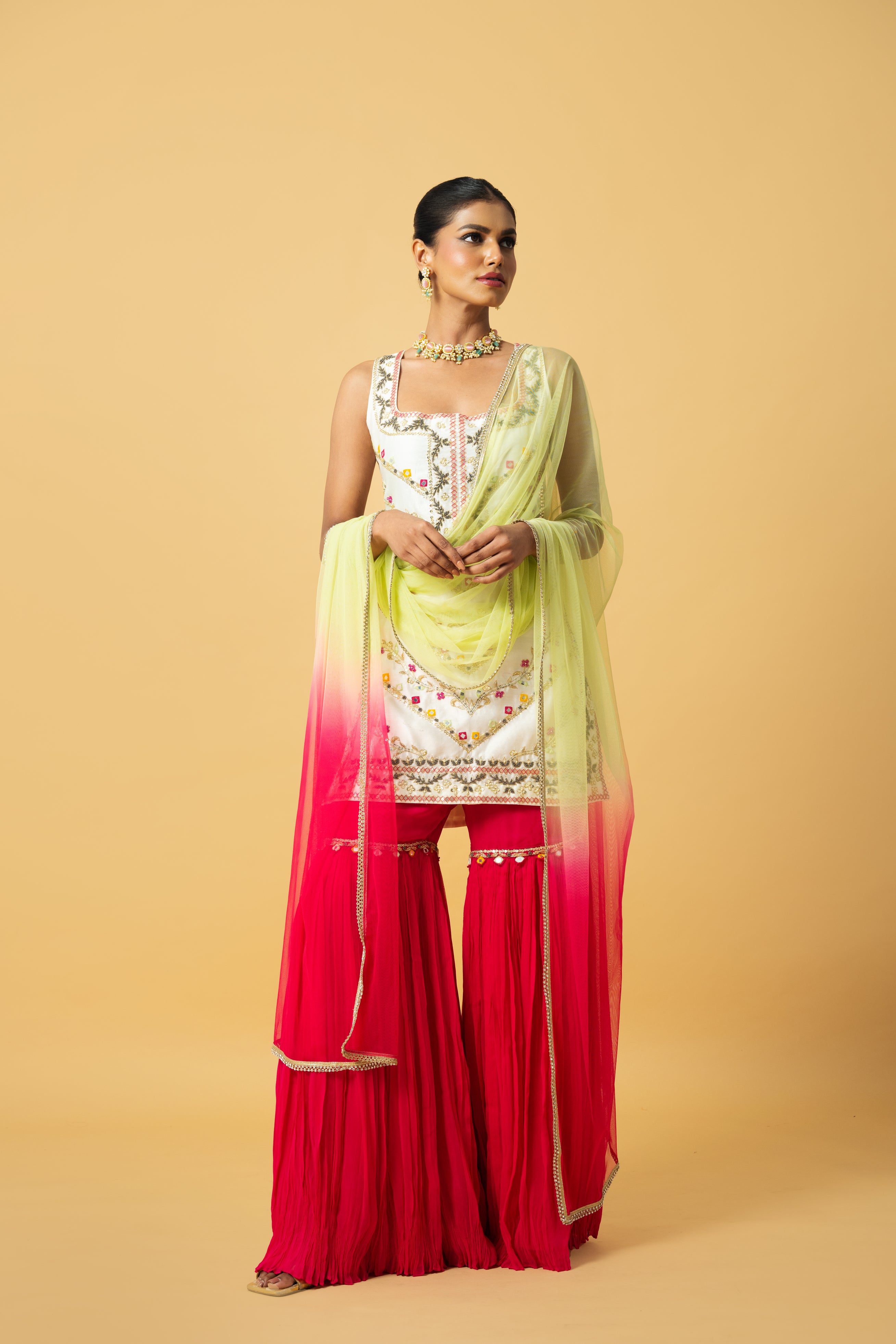 Ivory kurta with pink sharara and lime green dupatta featuring hand embroidery.