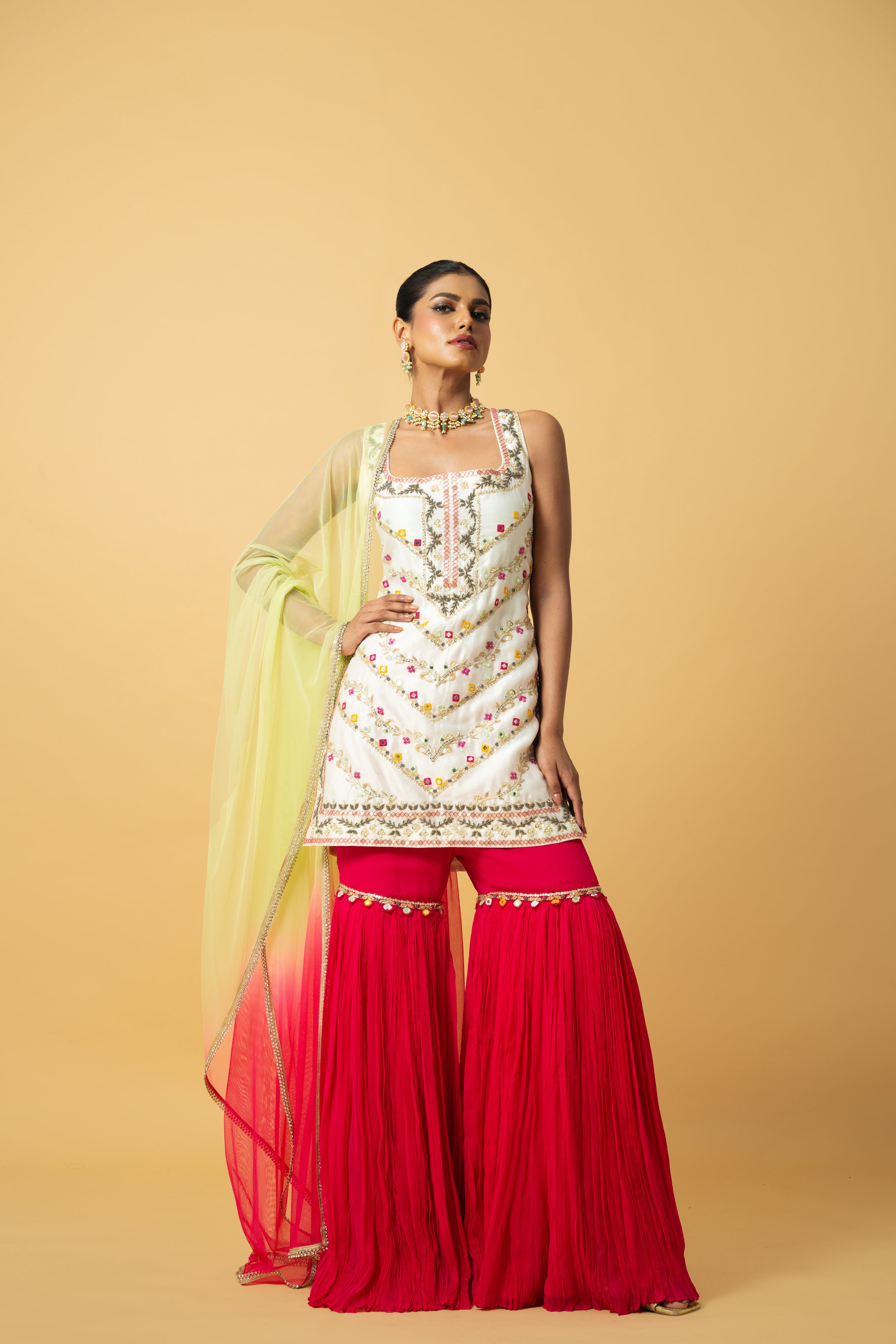 Ivory kurta with pink sharara and lime green dupatta featuring hand embroidery.