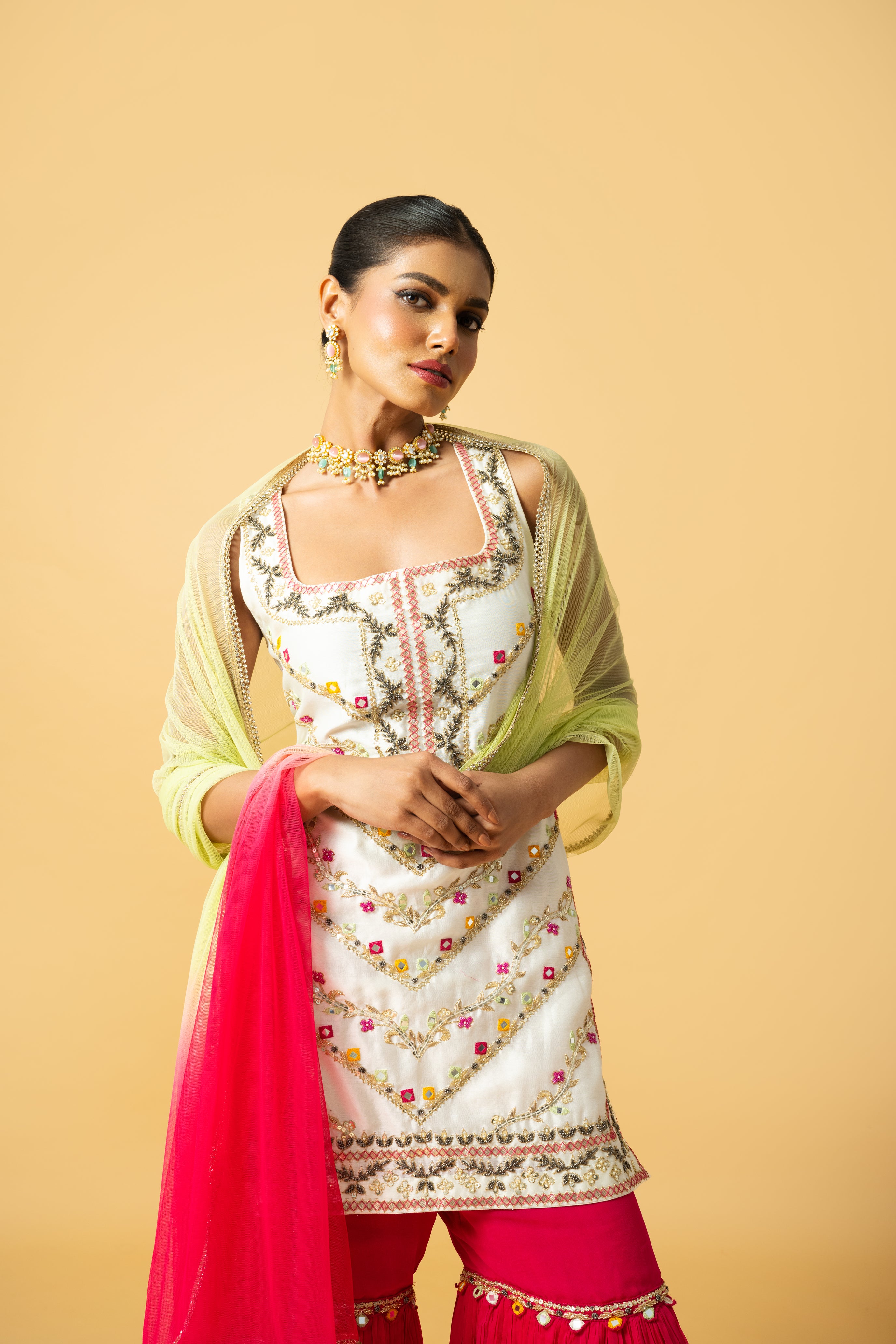 Ivory kurta with pink sharara and lime green dupatta featuring hand embroidery.