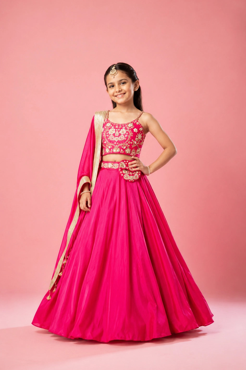 Hot pink lehenga set in modal satin with metal sleeves and a hand-embroidered heart-shaped pouch and belt. The dupatta is adorned with lace detailing for an extra touch of elegance.