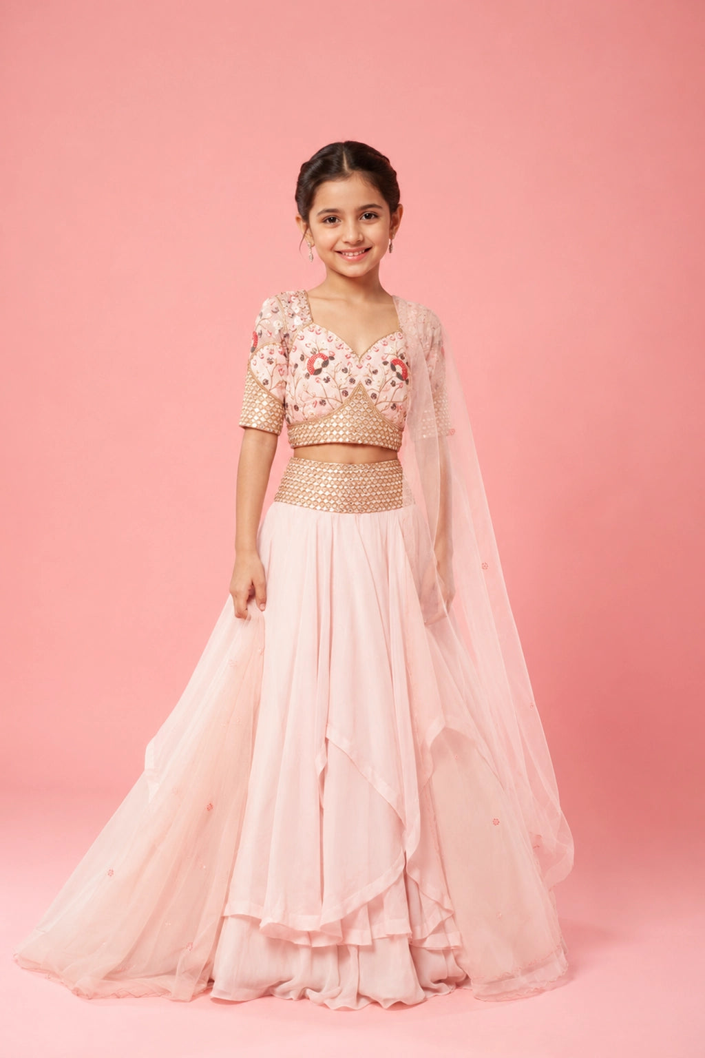 A baby pink layered lehenga crafted in organza, hand embroidery on the blouse, belt, and a soft net dupatta.