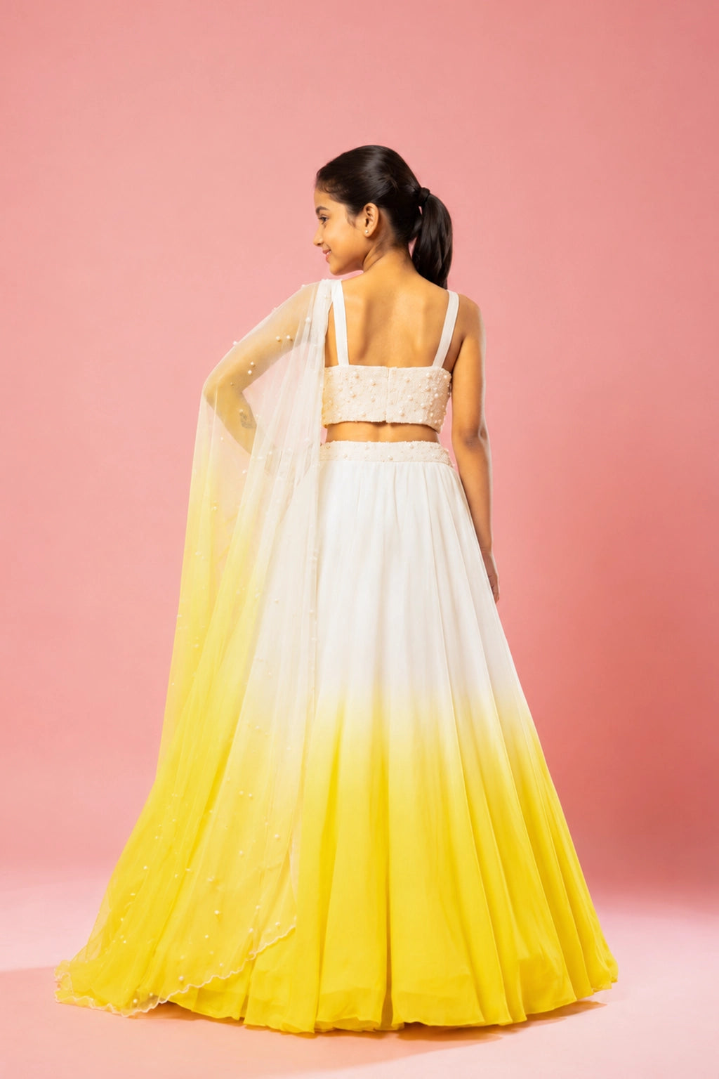 This ivory and sunshine yellow ombre lehenga in georgette is paired with a hand-embroidered blouse, belt, and soft net dupatta with pearl embellishments.