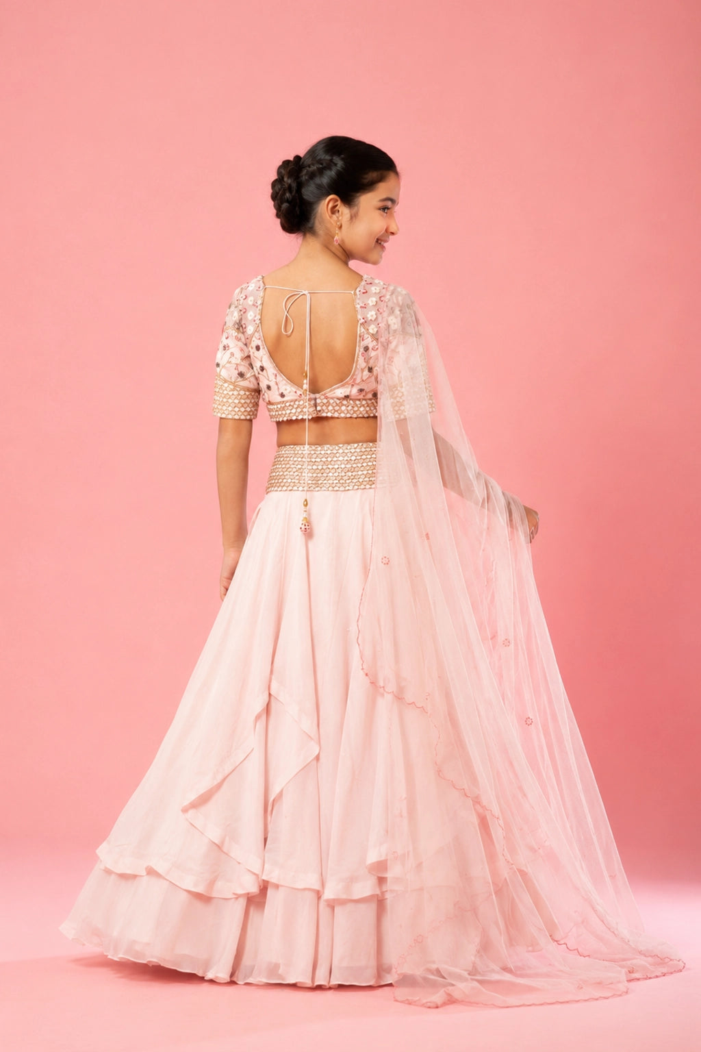 A baby pink layered lehenga crafted in organza, hand embroidery on the blouse, belt, and a soft net dupatta.